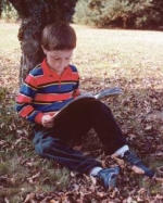 Foto: Junge sitzt lesend unter einem Baum